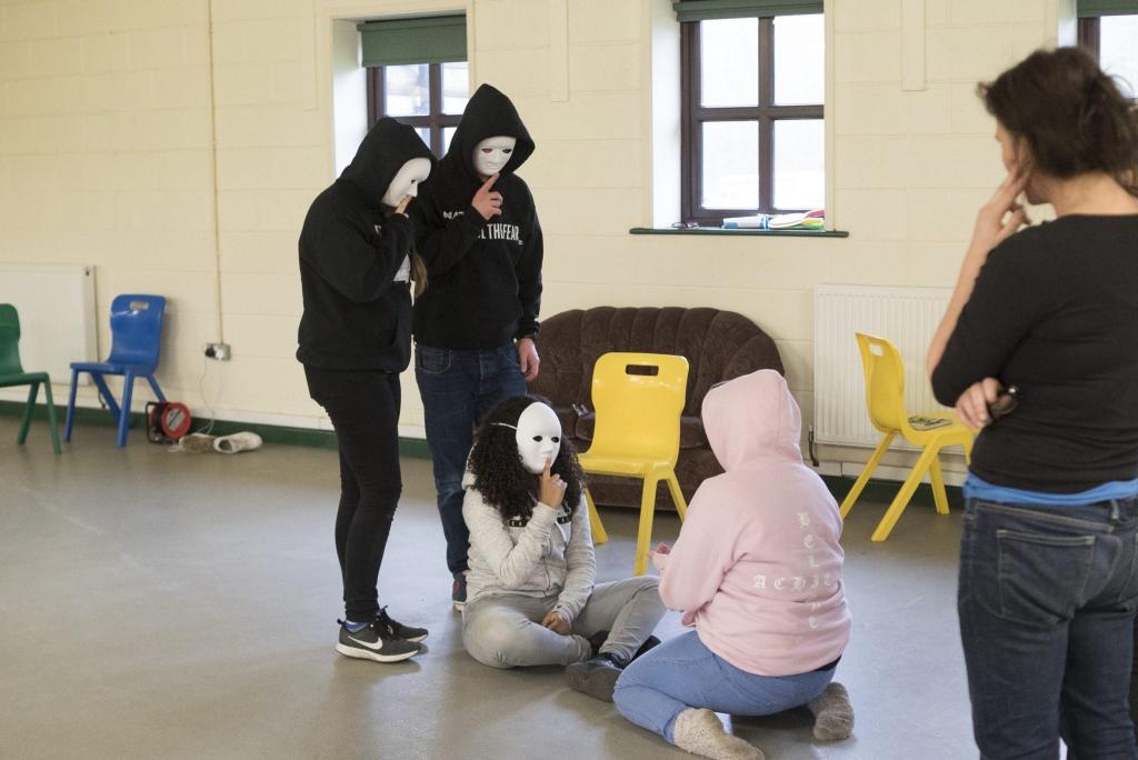 Four young people taking part in a drama session wearing white masks