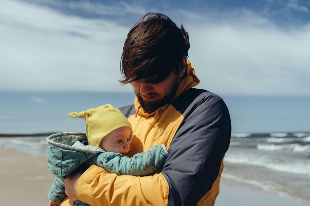 male foster carer holding baby at beach