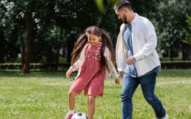 Young girl playing football with man in park representing long term fostering family